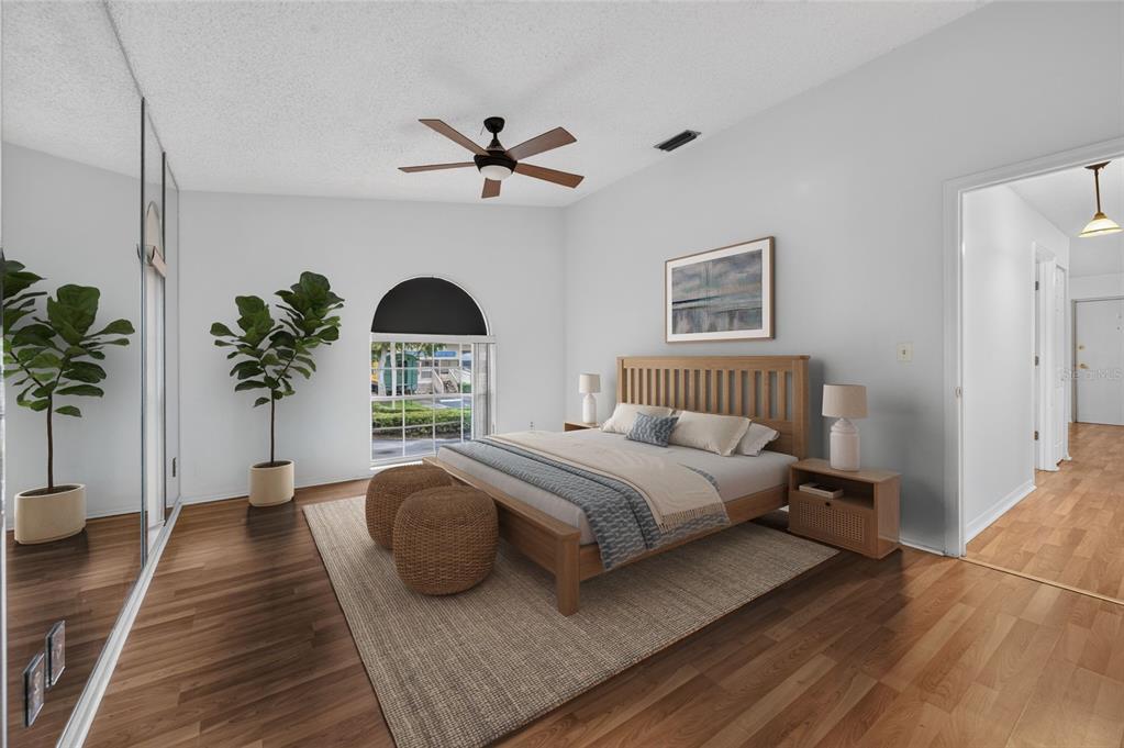 A bedroom with wood flooring, a wooden bed frame, a ceiling fan, and a large mirror — 689 WELLINGTON STATION BOULEVARD UNIT 50, ORMOND BEACH, FL