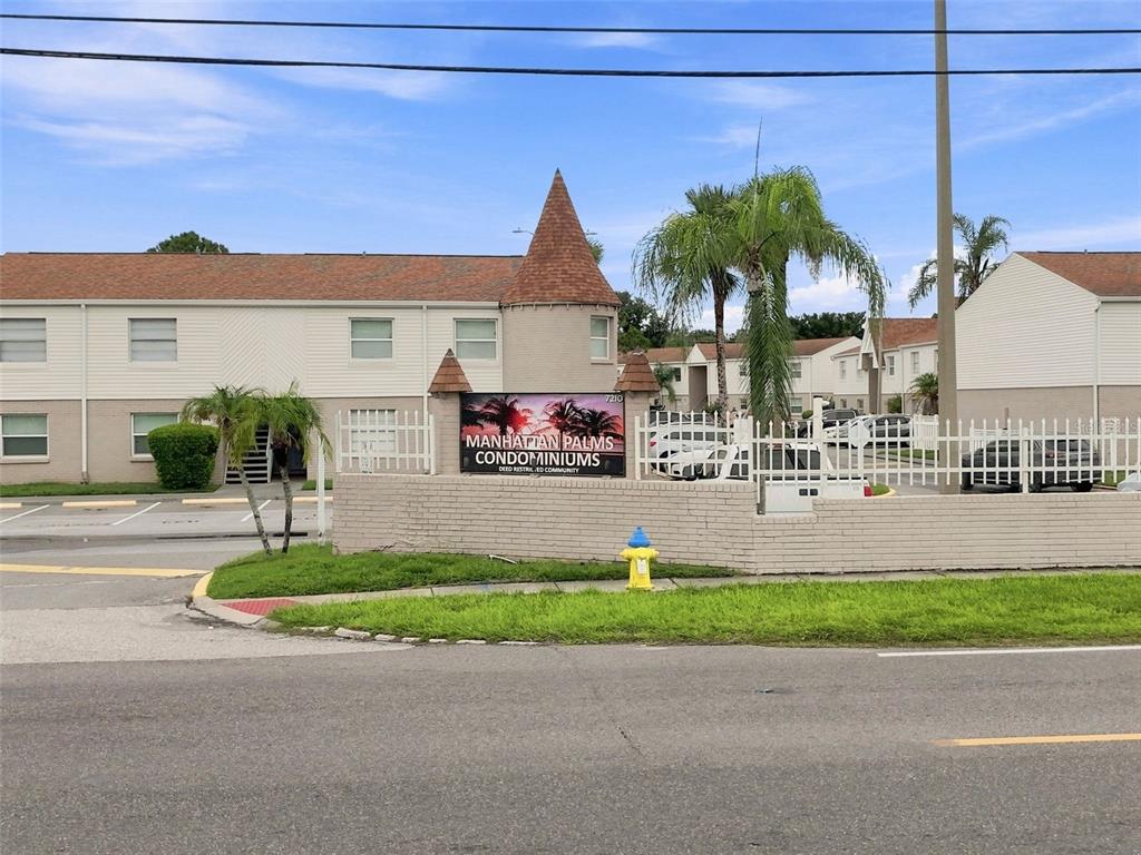 A sign for Manhattan Palms Condominiums stands in front of a two-story residential building — 7210 N MANHATTAN AVENUE UNIT 1014, TAMPA, FL