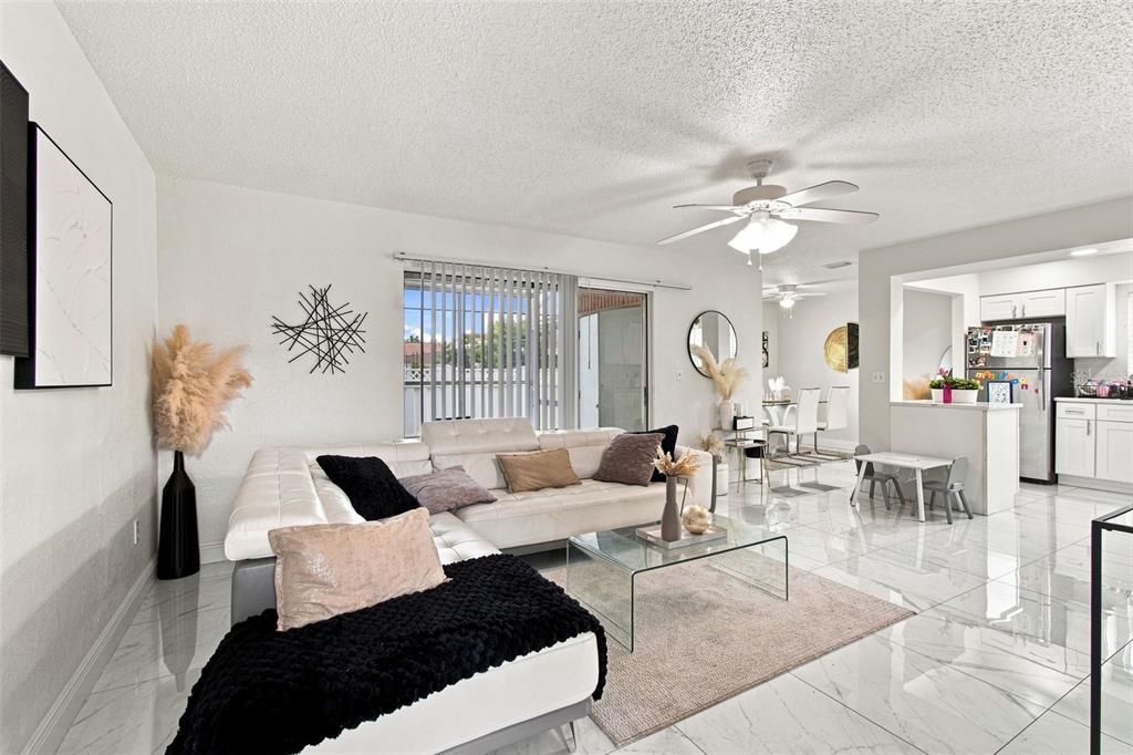 A bright living room features white tile floors, a sectional sofa, and an open kitchen — 7210 N MANHATTAN AVENUE UNIT 1014, TAMPA, FL