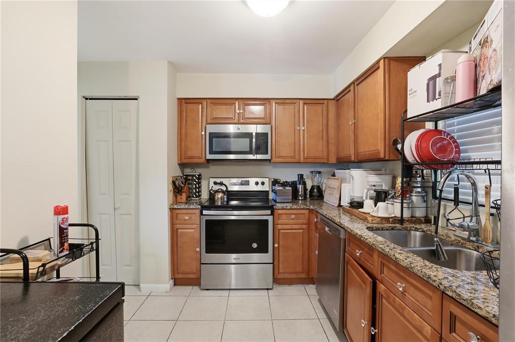 A kitchen features wood cabinets, granite countertops, stainless steel appliances, and light-colored tile flooring — 4915 PINE NEEDLE DRIVE, ORLANDO, FL