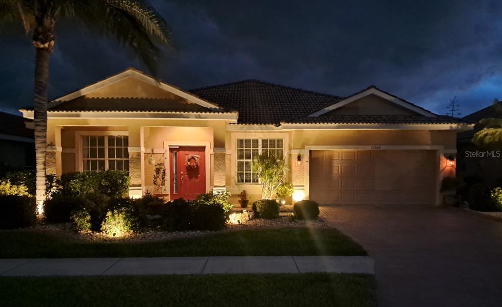 A single-story house with a red front door and a two-car garage at night — 11360 DANCING RIVER DRIVE, VENICE, FL