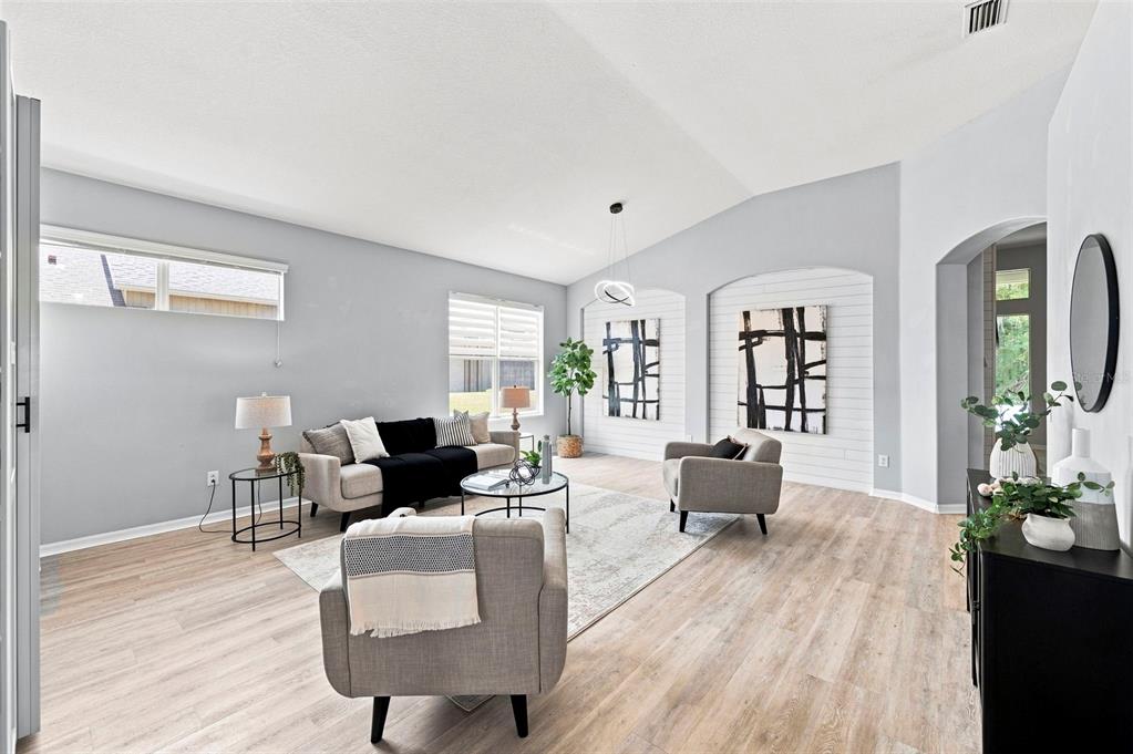 A bright living room features light wood flooring, gray walls, and two modern armchairs — 1501 FLATWOOD COURT, TRINITY, FL