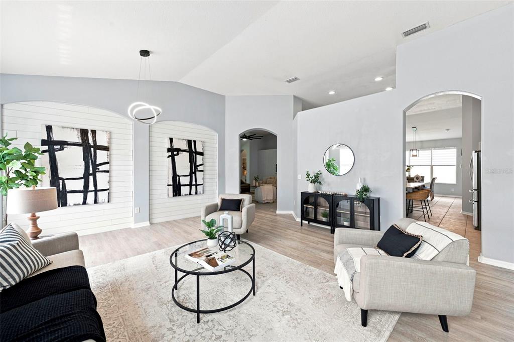 A bright living room features shiplap accent walls, modern artwork, and light wood-look flooring — 1501 FLATWOOD COURT, TRINITY, FL