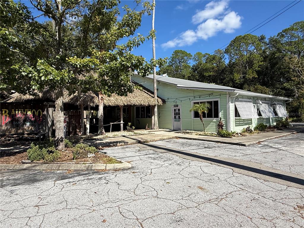 A light green building with a thatched-roof patio area sits next to a cracked parking lot — 1034 NW 57TH STREET, GAINESVILLE, FL