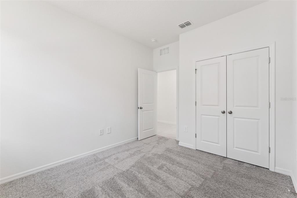 An empty bedroom features white walls, gray carpet, a closet with double doors, and an open doorway — 4275 DARBY COURT, EUSTIS, FL