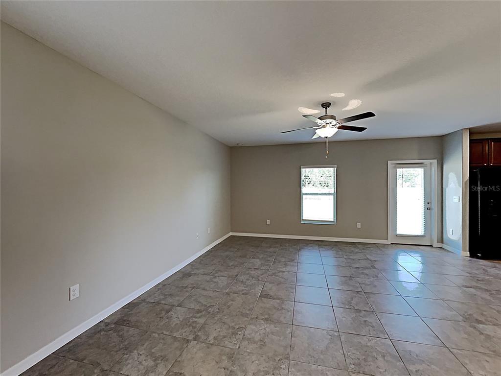 An empty living room features beige walls, large gray floor tiles, and a ceiling fan — 5125 WHITE CHICORY DRIVE, RUSKIN, FL