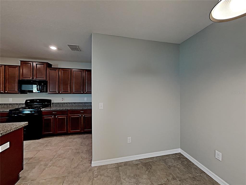 A kitchen with dark wood cabinets and granite countertops sits adjacent to a dining area — 5125 WHITE CHICORY DRIVE, RUSKIN, FL