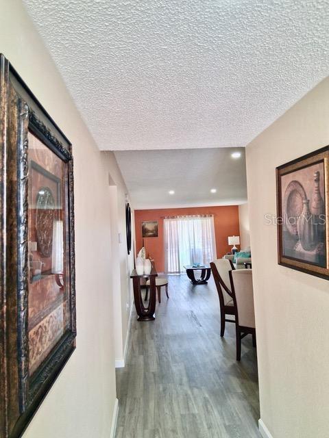 A hallway with framed artwork leads into a living area with light wood-look flooring — 4145 HERON WAY UNIT E-208, BRADENTON, FL