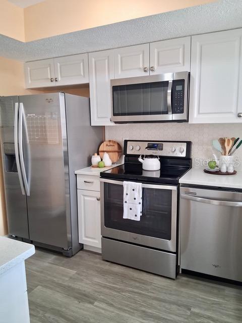A kitchen features white cabinets, stainless steel appliances, and light-colored wood-look flooring — 4145 HERON WAY UNIT E-208, BRADENTON, FL