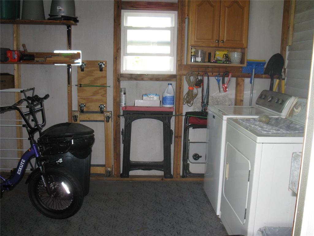 A laundry area in a garage with a washer, dryer, bike, and open wall shelving — 326 VICTORIA DRIVE, HAINES CITY, FL