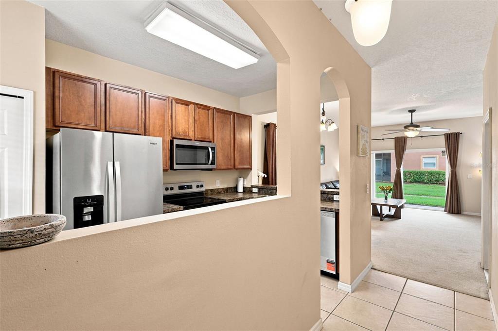 A kitchen with wood cabinets and stainless steel appliances overlooks a carpeted living area — 1360 LONG OAK WAY, SANFORD, FL