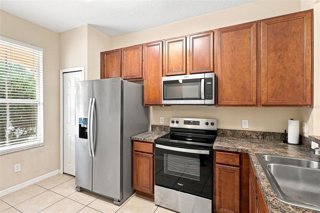 A kitchen with brown wooden cabinets, stainless steel appliances, and dark patterned laminate countertops — 1360 LONG OAK WAY, SANFORD, FL