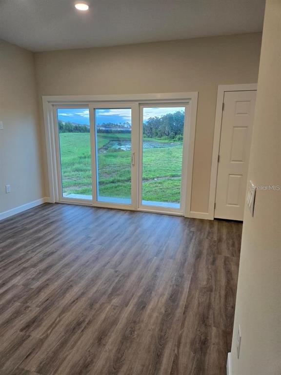An empty room with wood-look flooring, sliding glass doors, and a view of a pond — 1019 OAK BLUFF DRIVE, DAVENPORT, FL
