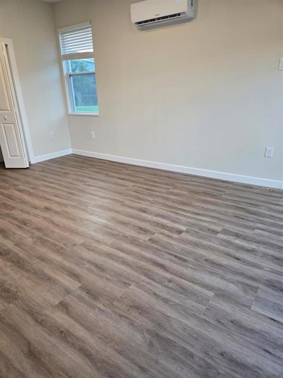 An empty room with light-colored walls, wood-look flooring, a window, and a wall-mounted air conditioner — 1019 OAK BLUFF DRIVE, DAVENPORT, FL