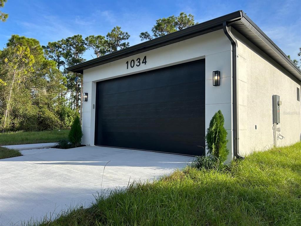 A modern detached garage with a black door and white stucco exterior — 1034 ALCALDE STREET E, LEHIGH ACRES, FL