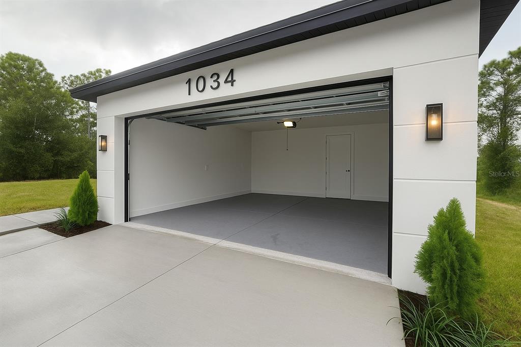A modern garage with white walls, a gray floor, and a single interior door — 1034 ALCALDE STREET E, LEHIGH ACRES, FL