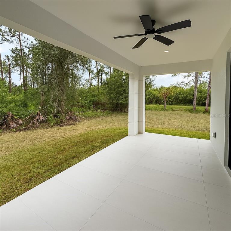A covered patio features white tile flooring, a ceiling fan, and a view of trees — 1034 ALCALDE STREET E, LEHIGH ACRES, FL