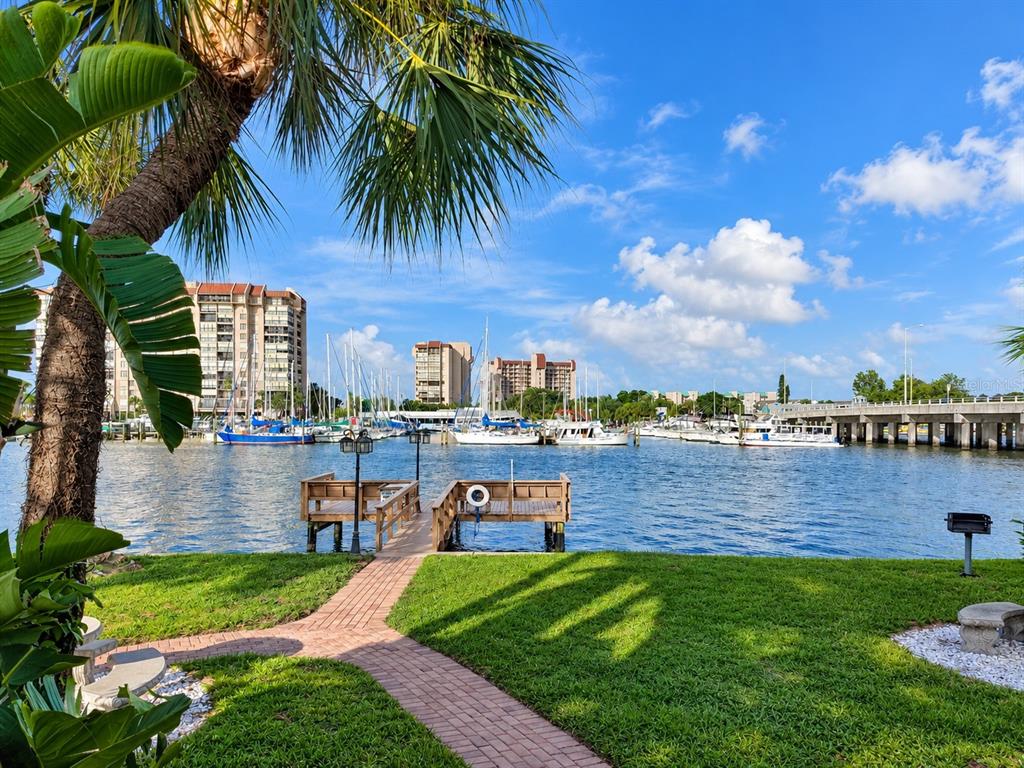 A grassy backyard features a picnic table, a wooden dock, and a view of boats — 9715 HARRELL AVENUE UNIT 14, TREASURE ISLAND, FL
