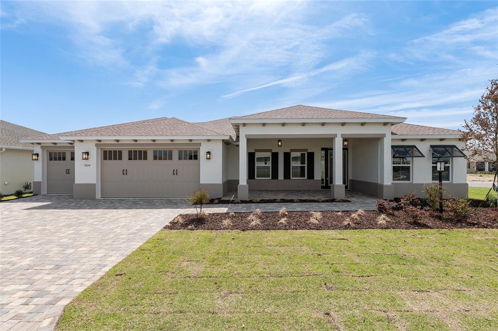 A single-story house with a beige stucco exterior, a paver driveway, and a three-car garage — 10154 SW 85TH PLACE ROAD, OCALA, FL