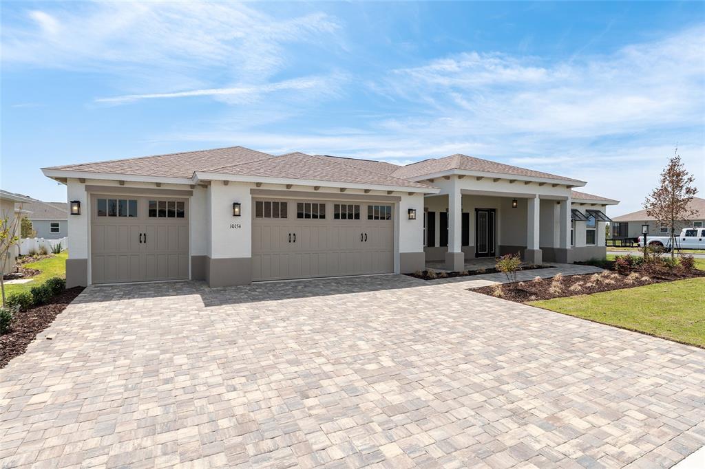 A single-story house with a three-car garage and a paved driveway under a blue sky — 10154 SW 85TH PLACE ROAD, OCALA, FL