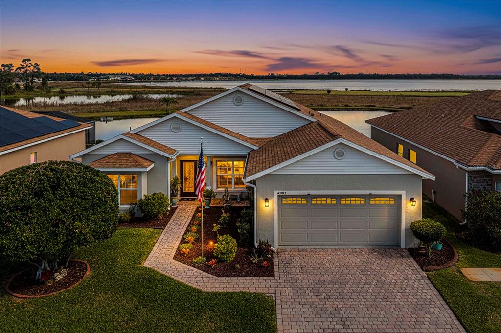 A single-story house with a paved driveway and walkway sits beside a lake at sunset — 4081 DUNMORE DRIVE, LAKE WALES, FL