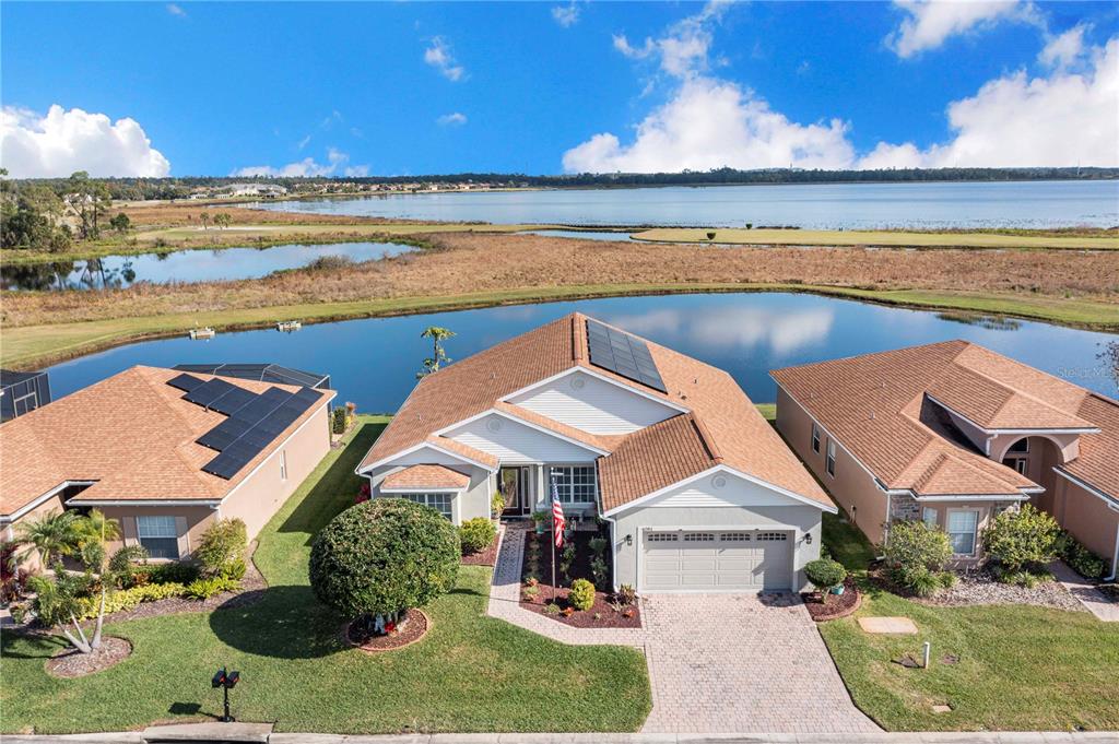 An aerial view shows a suburban house with solar panels, a garage, and a backyard pond — 4081 DUNMORE DRIVE, LAKE WALES, FL