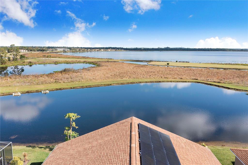An aerial view shows a house roof with solar panels overlooking a lake and wetlands — 4081 DUNMORE DRIVE, LAKE WALES, FL
