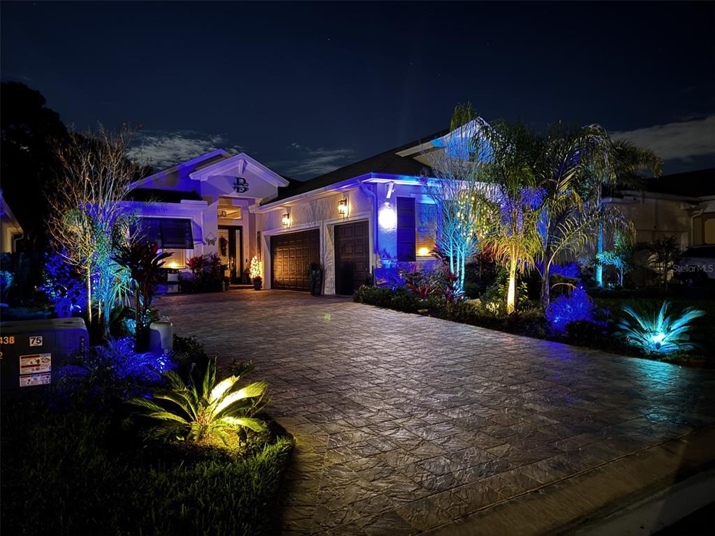 A paved driveway leads to a house illuminated by colorful landscape lighting at night — 20 SPRING STREET, PALM COAST, FL