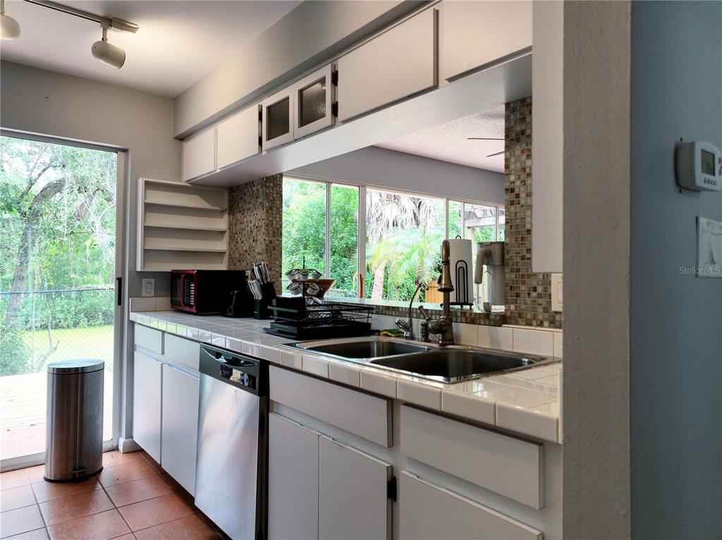 A kitchen features white cabinets, tiled countertops, a double sink, and a view of greenery — 111 OAK LEE DRIVE, LUTZ, FL