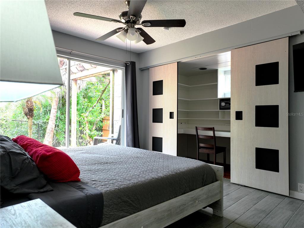 A bedroom features a bed, a ceiling fan, sliding doors to a workspace, and patio access — 111 OAK LEE DRIVE, LUTZ, FL
