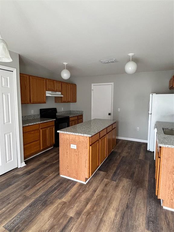 A kitchen features wood cabinets, granite countertops, a central island, and dark wood-look flooring — 11102 SUMMER STAR DRIVE, RIVERVIEW, FL