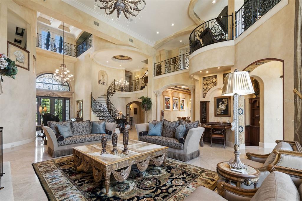 A grand living room features a curved staircase, ornate chandeliers, and a two-story balcony — 2961 LAKEVIEW DRIVE, SEBRING, FL
