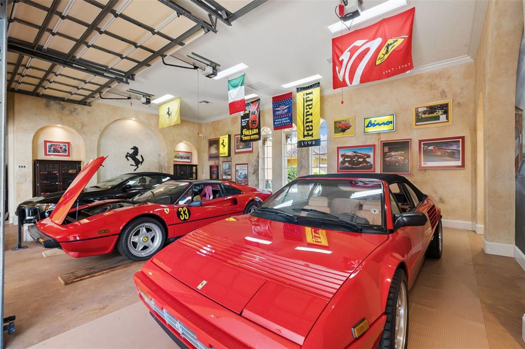 A garage with beige walls, Ferrari memorabilia, and two red sports cars parked inside — 2961 LAKEVIEW DRIVE, SEBRING, FL