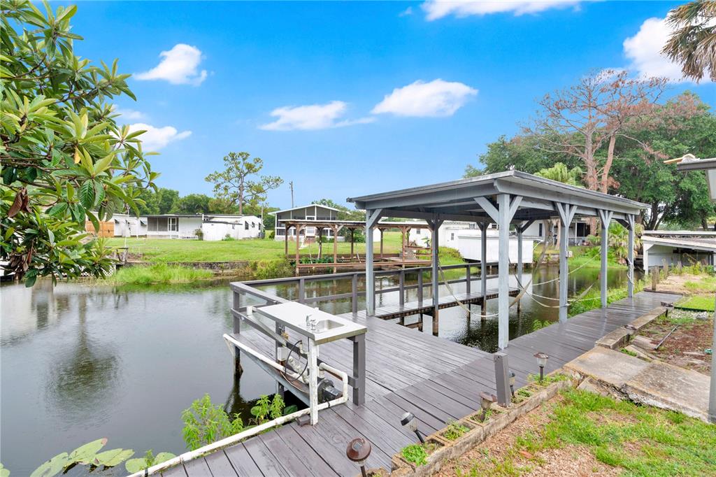 A wooden boat dock with a covered slip sits over a canal near several homes — 13450 PALM DRIVE, ASTATULA, FL