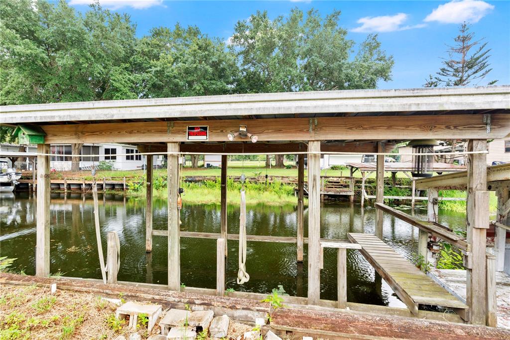 A wooden boat dock with a metal roof sits over a canal — 13450 PALM DRIVE, ASTATULA, FL