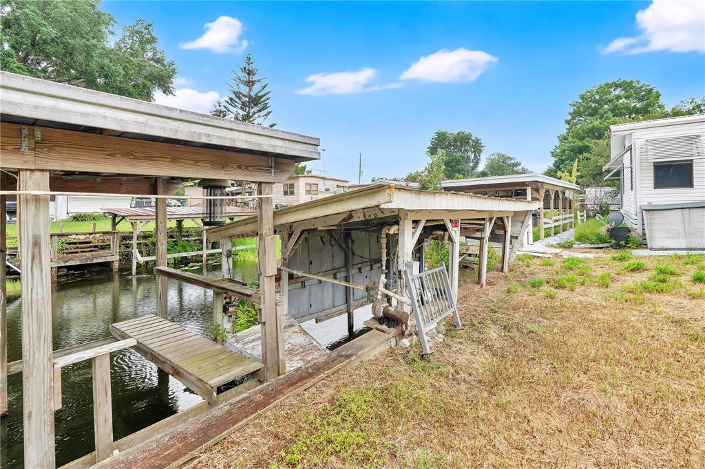 A wooden boat dock and covered slip sit along a canal next to a mobile home — 13450 PALM DRIVE, ASTATULA, FL