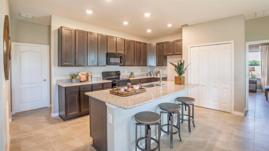 A kitchen features dark wood cabinets, granite countertops, a central island, and tile flooring — 1927 TRAVELERS PALM DRIVE, EDGEWATER, FL
