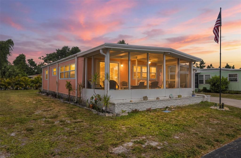 A peach-colored mobile home with a screened-in porch and an American flag in the yard — 24437 HARBORVIEW ROAD UNIT 5, PUNTA GORDA, FL