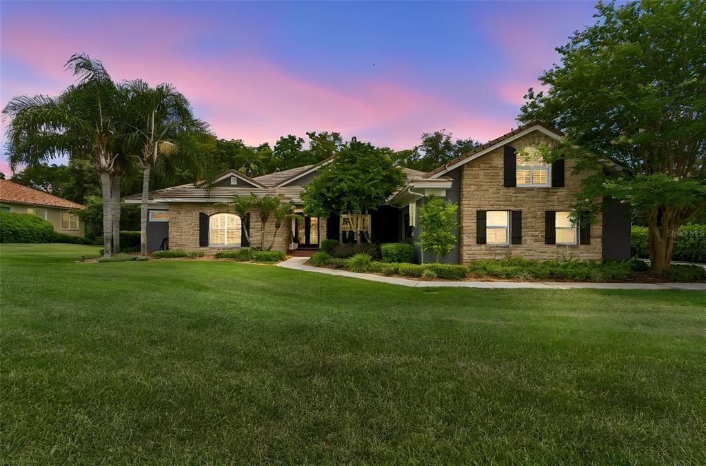 A stone-faced house with a large lawn and palm trees under a sunset sky — 12716 TRADITION DRIVE, DADE CITY, FL