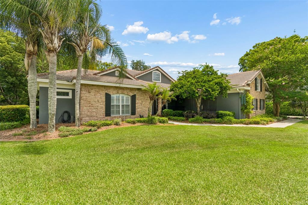 A single-story house with a stone facade and a large front lawn under a blue sky — 12716 TRADITION DRIVE, DADE CITY, FL