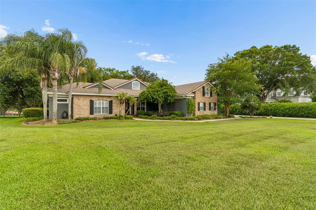 A stone-faced house with black shutters sits behind a large tree on a grassy lawn — 12716 TRADITION DRIVE, DADE CITY, FL
