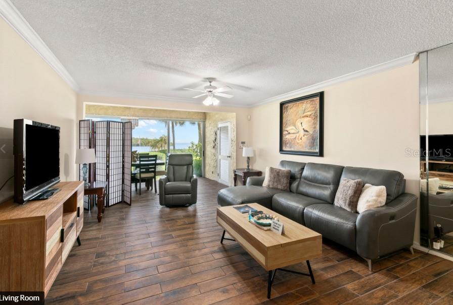 A living room with wood-look tile flooring, a gray sectional sofa, and a water view — 605 SUTTON PLACE UNIT 102, LONGBOAT KEY, FL