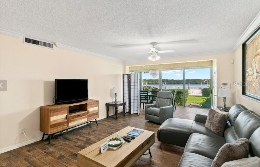 A living room features a television console, leather sectional, and sliding doors overlooking a lake — 605 SUTTON PLACE UNIT 102, LONGBOAT KEY, FL