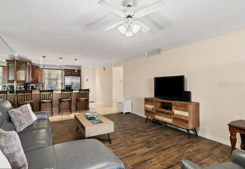 A living room with wood-look tile flooring, a ceiling fan, and an open kitchen area — 605 SUTTON PLACE UNIT 102, LONGBOAT KEY, FL