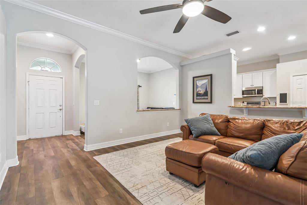 A living room with wood-look flooring, a brown leather sectional, and an arched wall cutout — 242 BLUE WATER STREET, EUSTIS, FL
