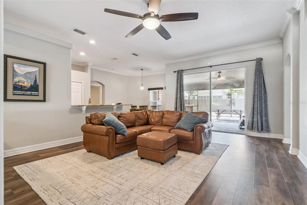 A living room features a brown leather sectional, a patterned rug, and sliding glass doors — 242 BLUE WATER STREET, EUSTIS, FL