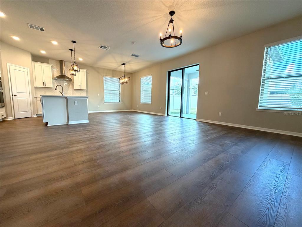 An open-concept kitchen features white cabinetry, a central island, and wood-look flooring — 9872 AUREA MOSS LANE, ORLANDO, FL