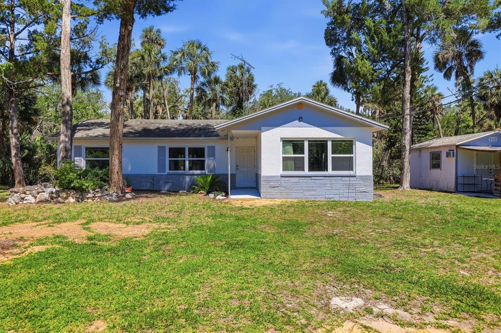A single-story house with white siding, a gray stone base, and a detached shed nearby — 6244 COLONY CIRCLE, WEEKI WACHEE, FL