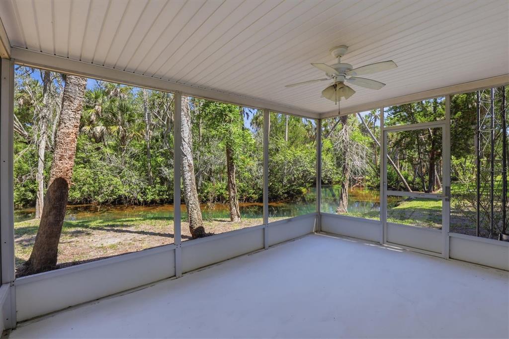 A screened-in porch with a ceiling fan overlooks a wooded area and a small stream — 6244 COLONY CIRCLE, WEEKI WACHEE, FL