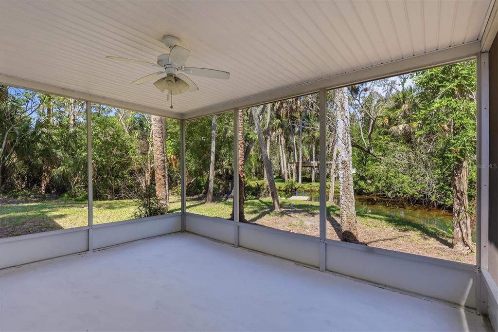 A screened-in porch features a white ceiling fan and views of a wooded backyard and creek — 6244 COLONY CIRCLE, WEEKI WACHEE, FL